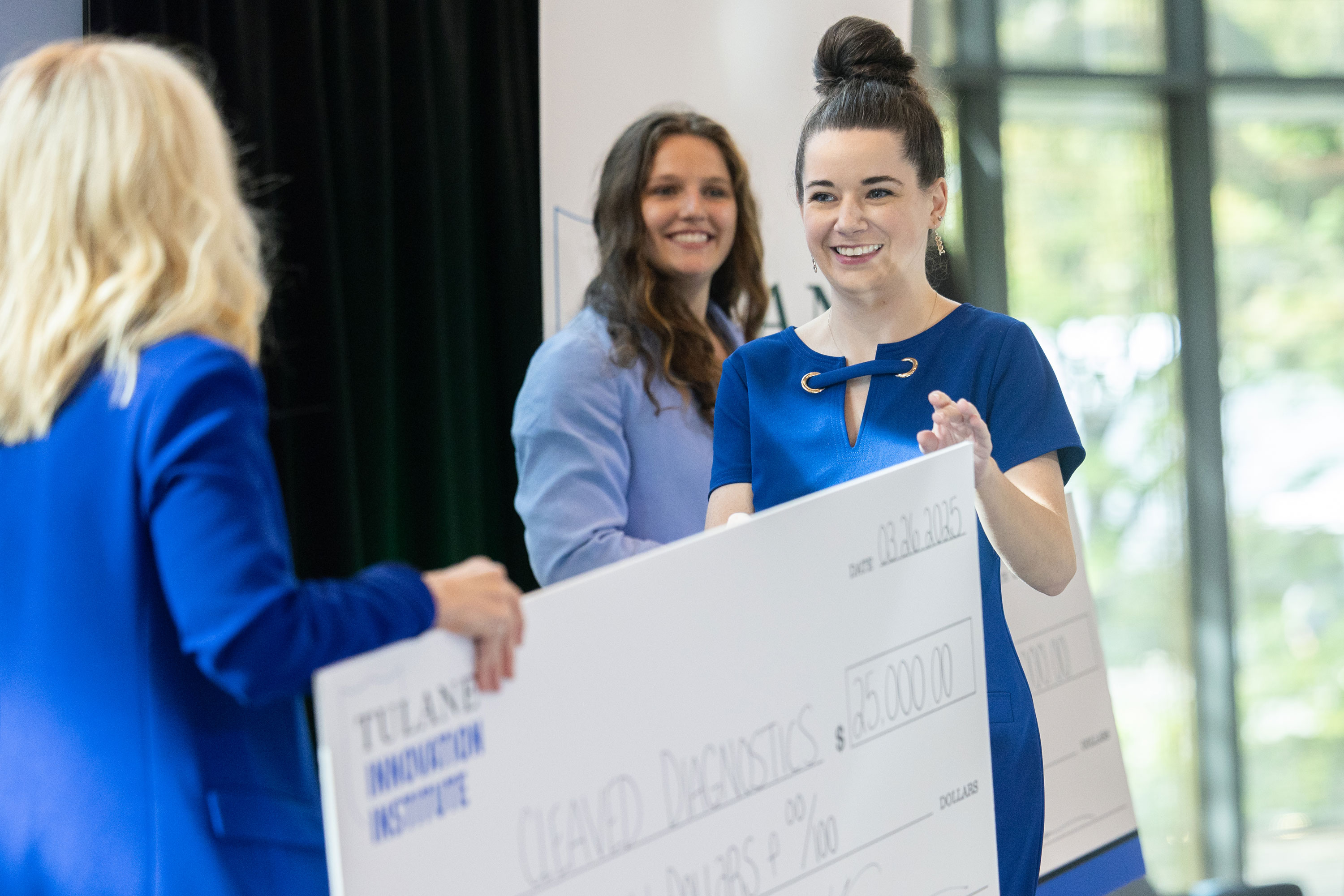 Smiling women receive a large novelty check from the Tulane Innovation Institute.