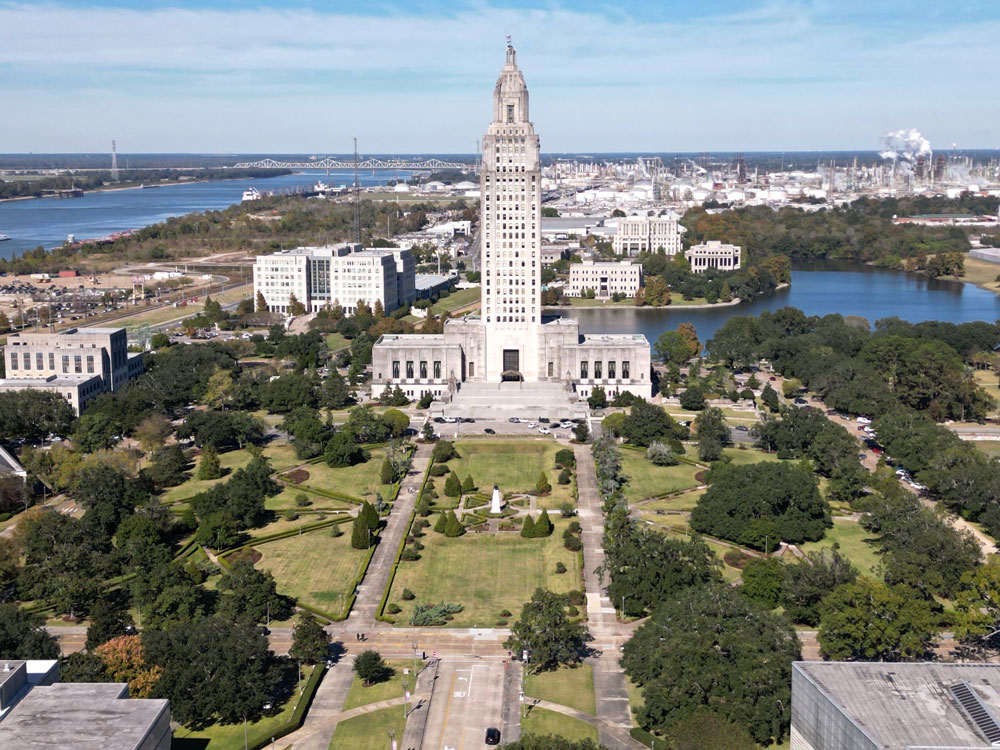 Aerial view of the Louisiana State Capitol, a towering Art Deco building with gardens and water.