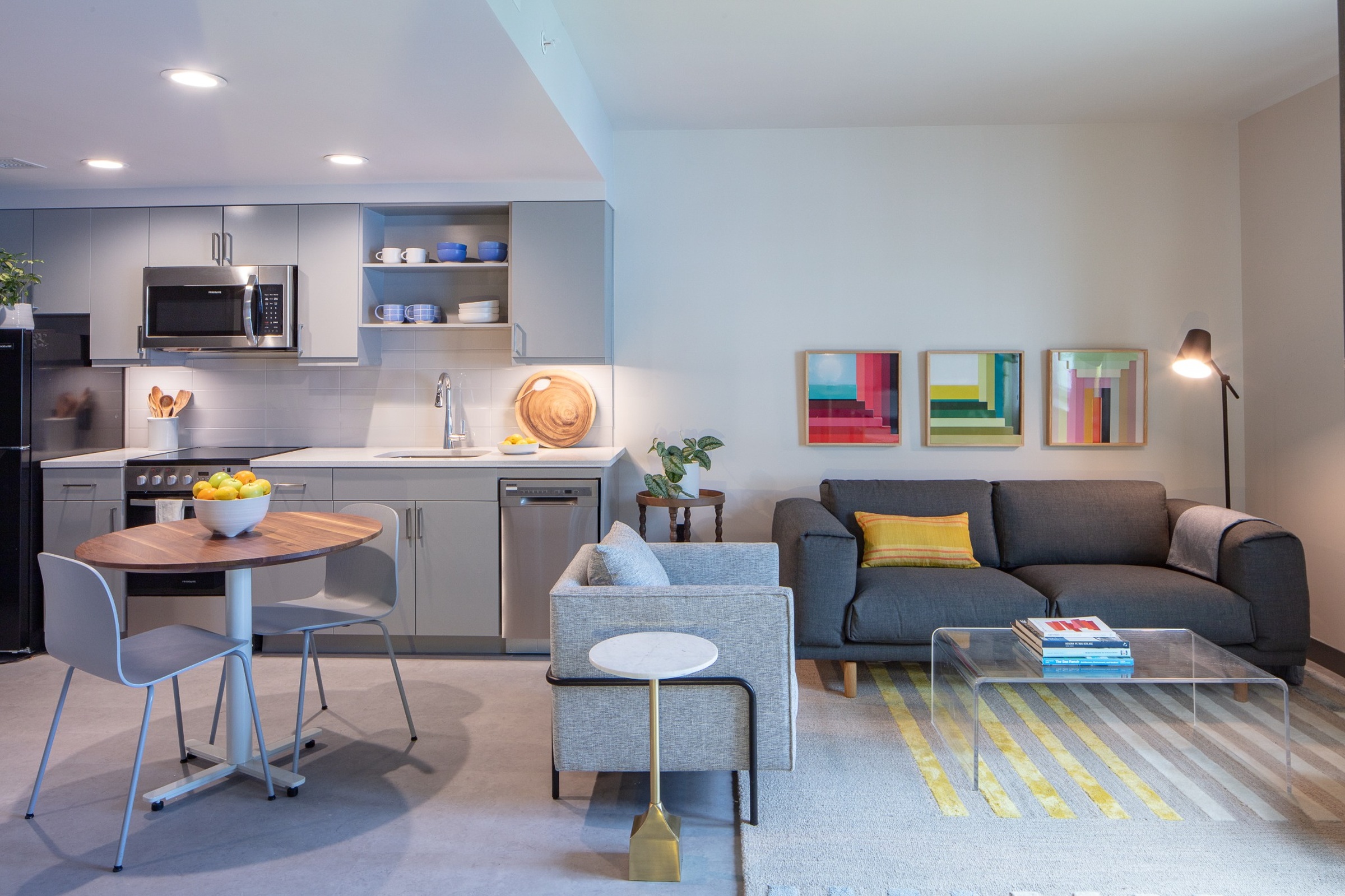Modern open-plan kitchen and living room with grey furniture and colorful art.